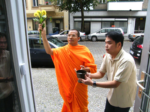 Der buddhistische Mönch segnet den Eingang zum neuen Musik-Cafe in Berlin-Neukölln - DJ Pön reicht die Schale mit dem heiligen Wasser.